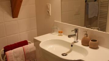 A bathroom with a white sink, mirror, and wooden beams. There is a towel rack with a red towel and a white towel.