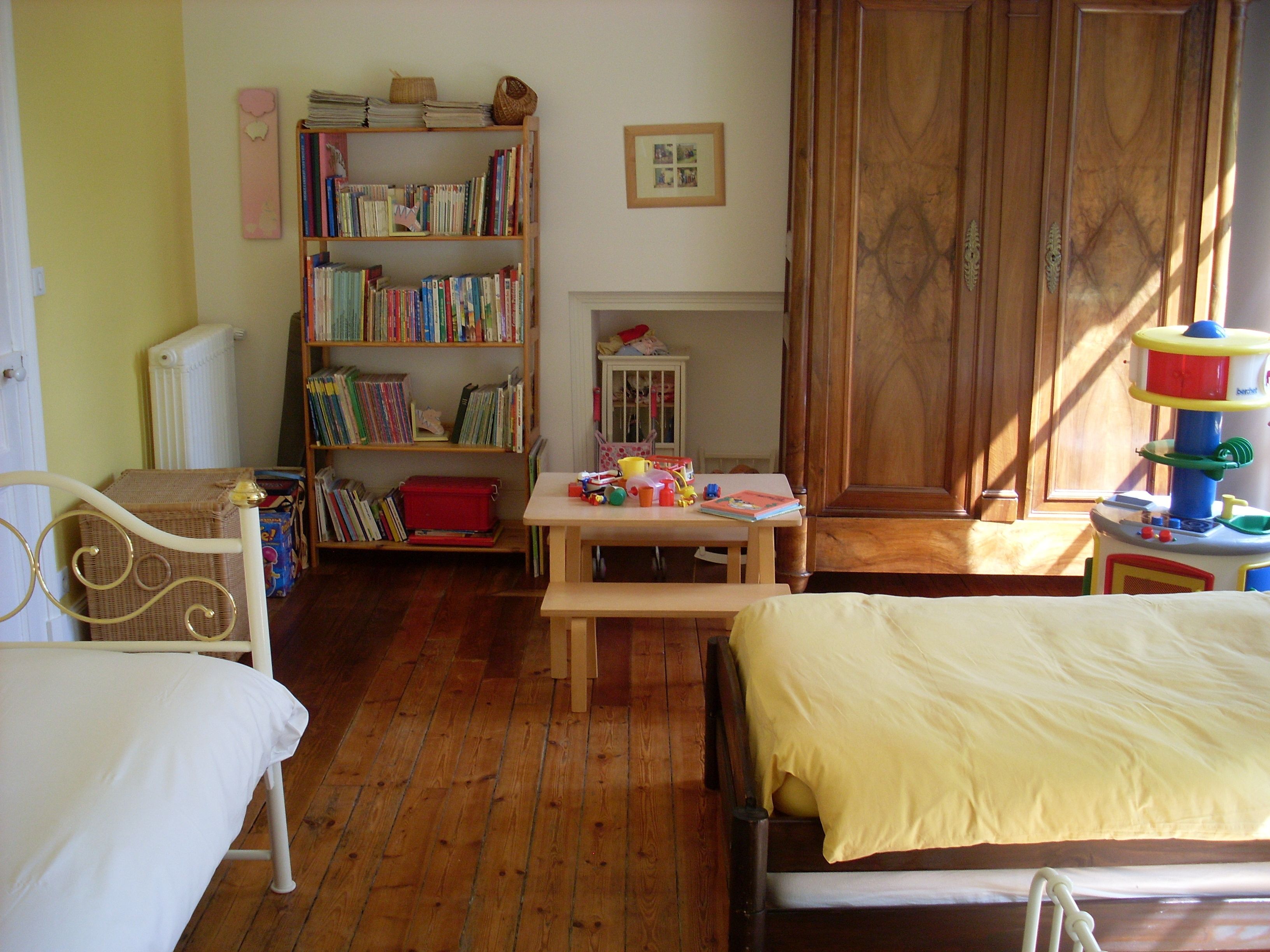 A room with a bed, a wooden desk, a bookshelf, and a window with curtains.