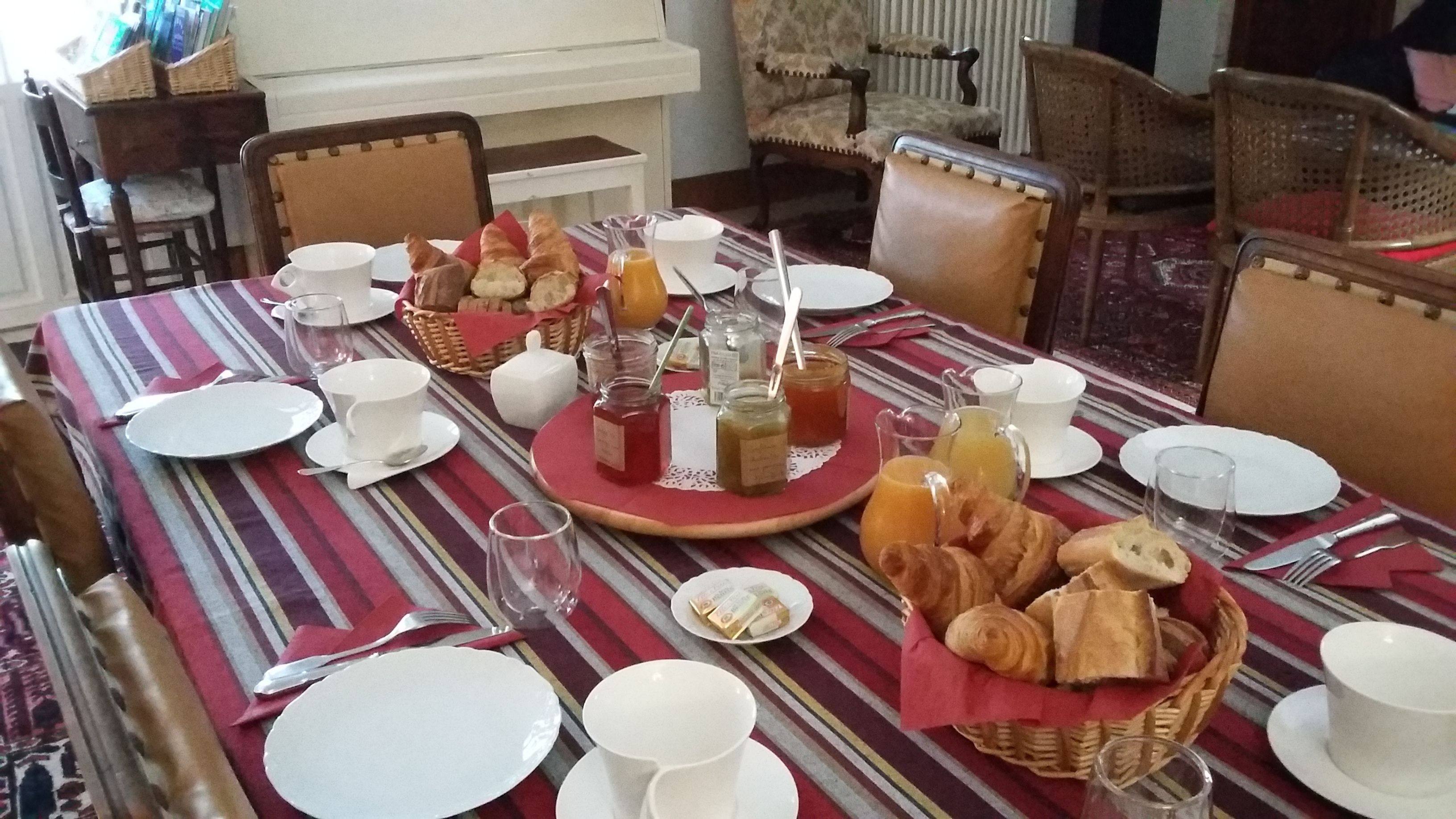 A dining table set with plates, cups, and a basket of bread.