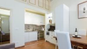 Una cocina compacta con armarios blancos, una mesa de comedor y una silla.