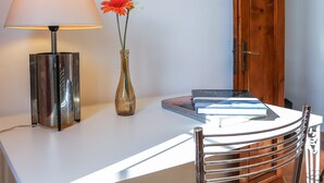 Une pièce avec un bureau blanc, une lampe, un vase de fleurs et une porte.