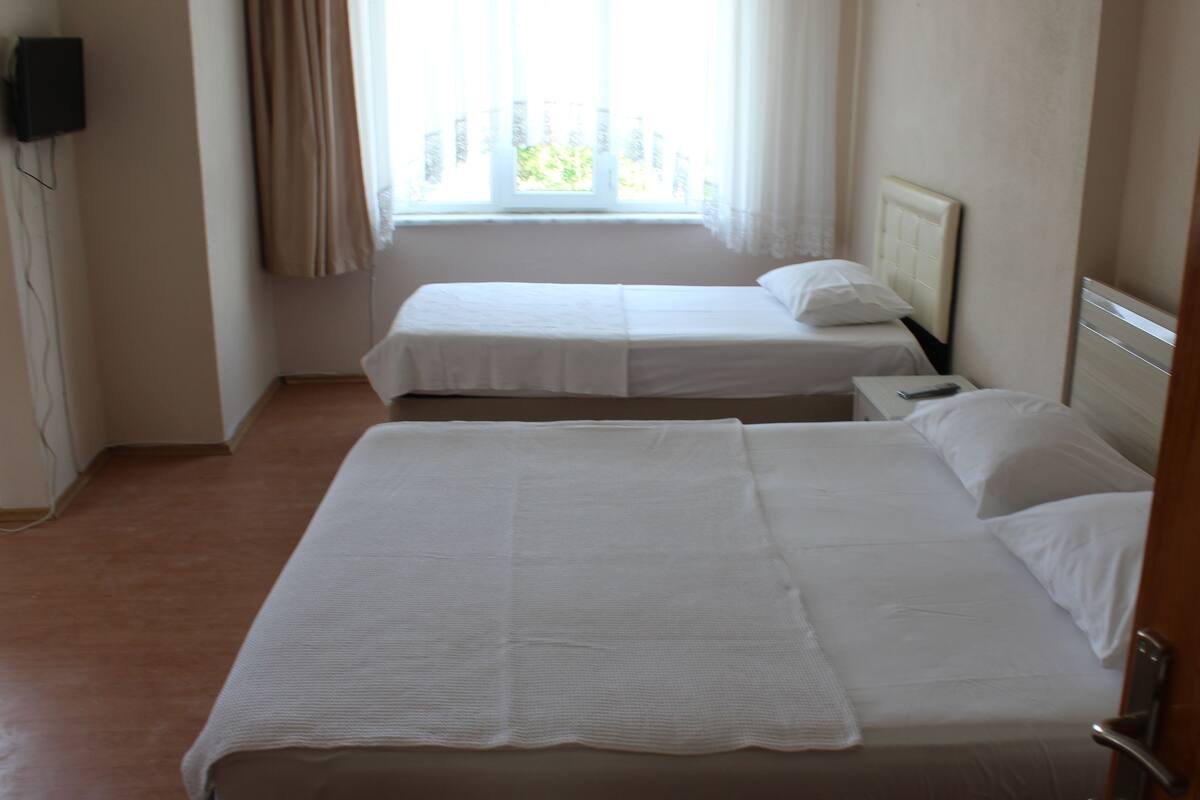 A hotel room with two single beds, a bedside table with a remote control, and a window with curtains.
