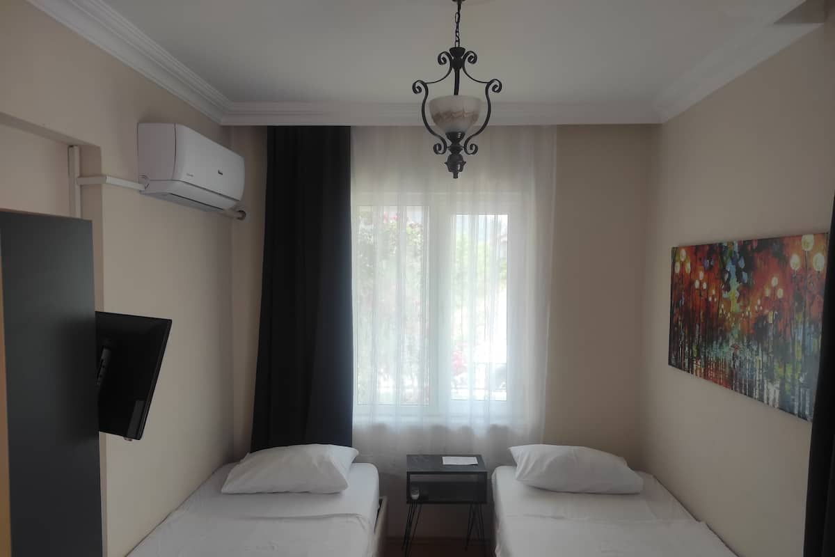 A hotel room with two beds, a desk, a TV, an air conditioner, a chandelier, and a painting on the wall.