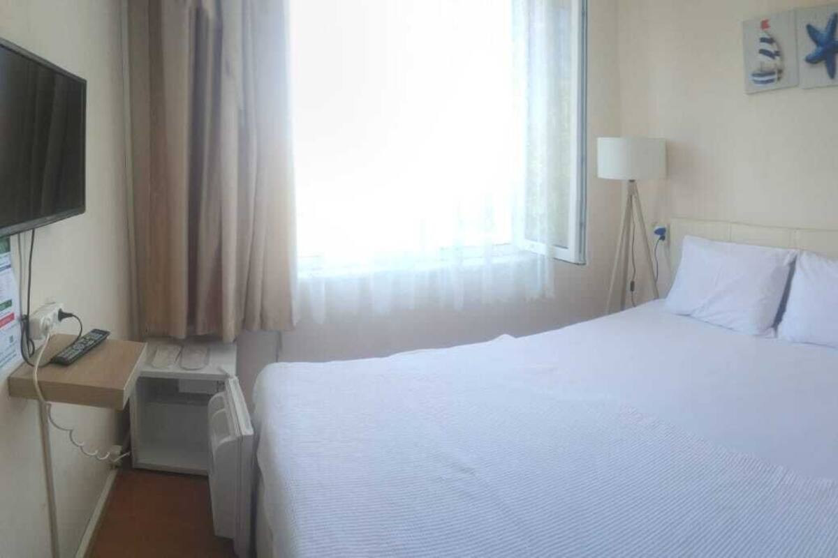A hotel room with a large bed, a desk with a computer, a TV, and a window with curtains.