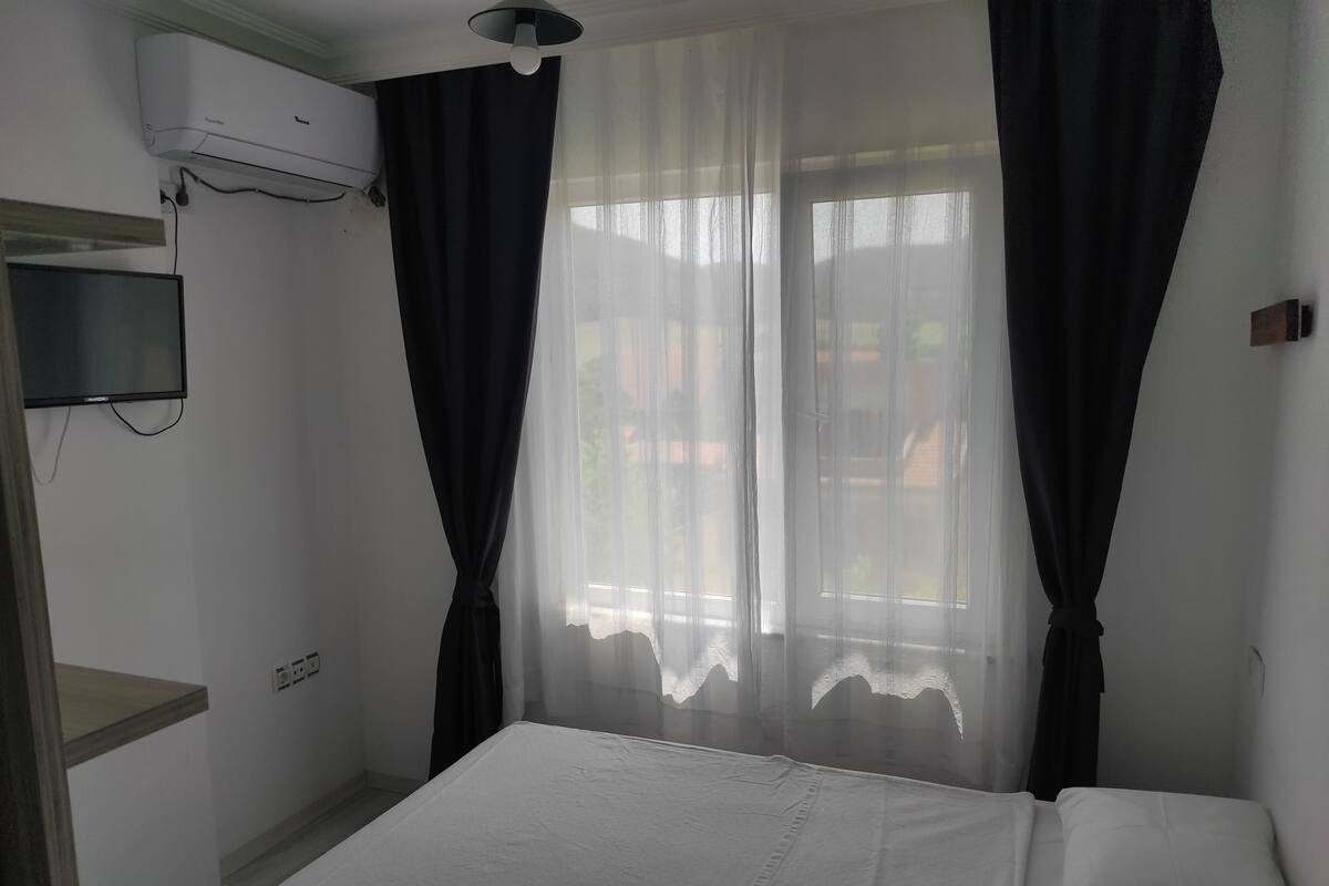 A hotel room with a bed, a TV mounted on the wall, and an air conditioning unit.