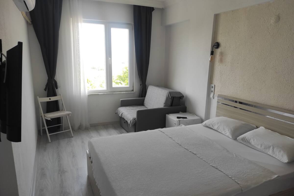 A bedroom with a bed, a chair, a small table, and a window with curtains.