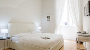 Une chambre à coucher bien rangée, avec un lit, des tables de chevet, une lampe, un tableau encadré et une fenêtre avec des rideaux.