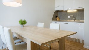 Une cuisine moderne avec des meubles blancs, une table à manger en bois et un luminaire suspendu.