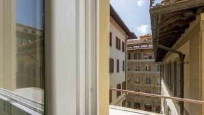 Une rue étroite, bordée de bâtiments des deux côtés, un balcon avec une balustrade et une fenêtre dans laquelle se reflètent les bâtiments.