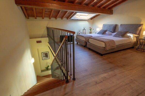 Une chambre avec une lucarne, deux lits, un escalier et une petite table avec une lampe.
