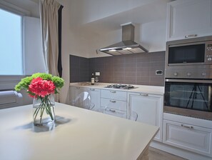 A modern kitchen with white cabinets, a gas stove, a built-in oven, and a window with curtains.