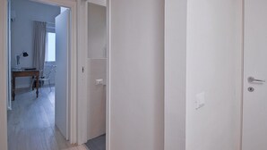 A hallway with wooden flooring, a door on the right, and an open door leading to a room with a desk and chair. - Borgo dei Greci (Florence)