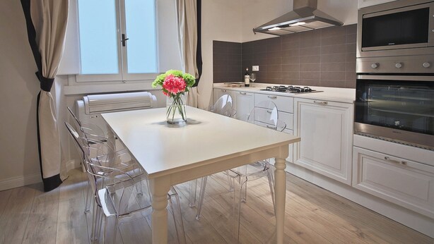 A modern kitchen with white cabinets, a stainless steel oven, and a dining table with clear chairs. - Borgo dei Greci (Florence)