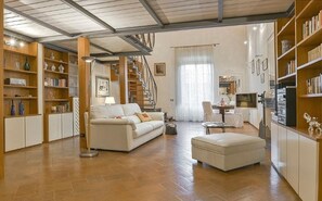 A spacious living room with a white sofa, a coffee table, and a bookshelf filled with books. A staircase is visible in the background, leading to an upper floor. - Canova (Florence)
