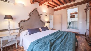 Une chambre avec un grand lit, des poutres en bois au plafond, une table de chevet avec une lampe et un miroir au-dessus du lit.