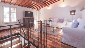 Un vaste espace de vie agrémenté d’un escalier en bois, d’un téléviseur à écran plat, d’un canapé blanc et d’une lampe.