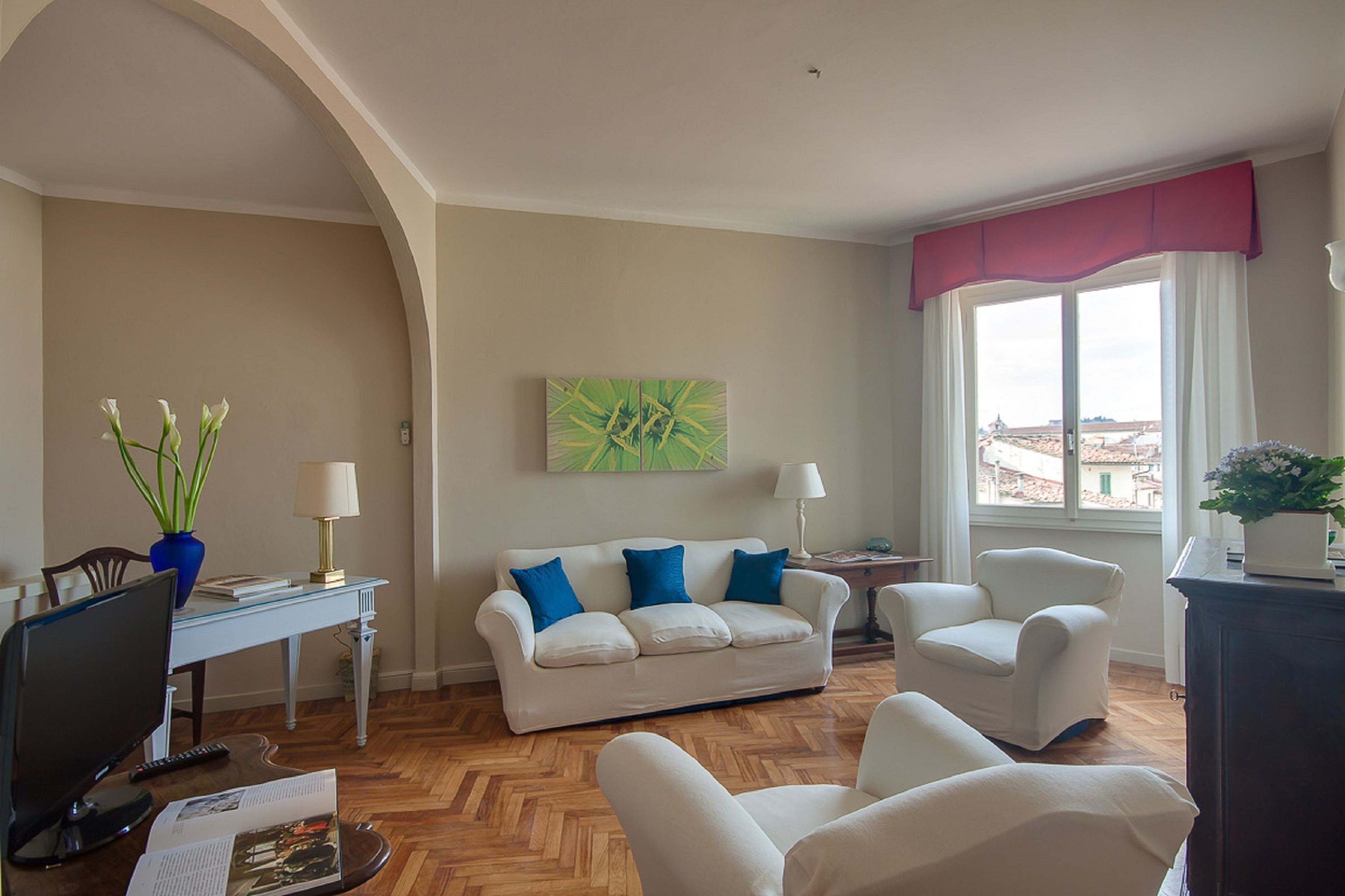Ein Wohnzimmer mit einem weißen Sofa, zwei Sesseln, einem Couchtisch, einem Fernseher und einem Bücherregal.
