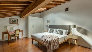 A bedroom with a wooden ceiling, a bed with pillows, a bedside table with a lamp, and a desk with a chair. - Federighi Loft (Florence)