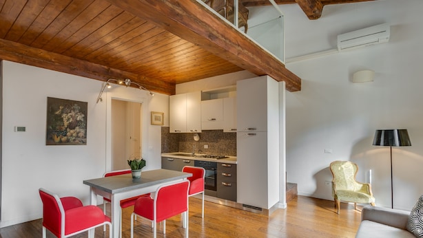 A modern kitchen with white cabinets and a granite countertop, a dining area with red chairs, and a wooden ceiling. - Federighi Loft (Florence)