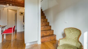 A staircase with wooden steps, a red chair, and a green armchair in a room with wooden flooring and white walls. - Federighi Loft (Florence)