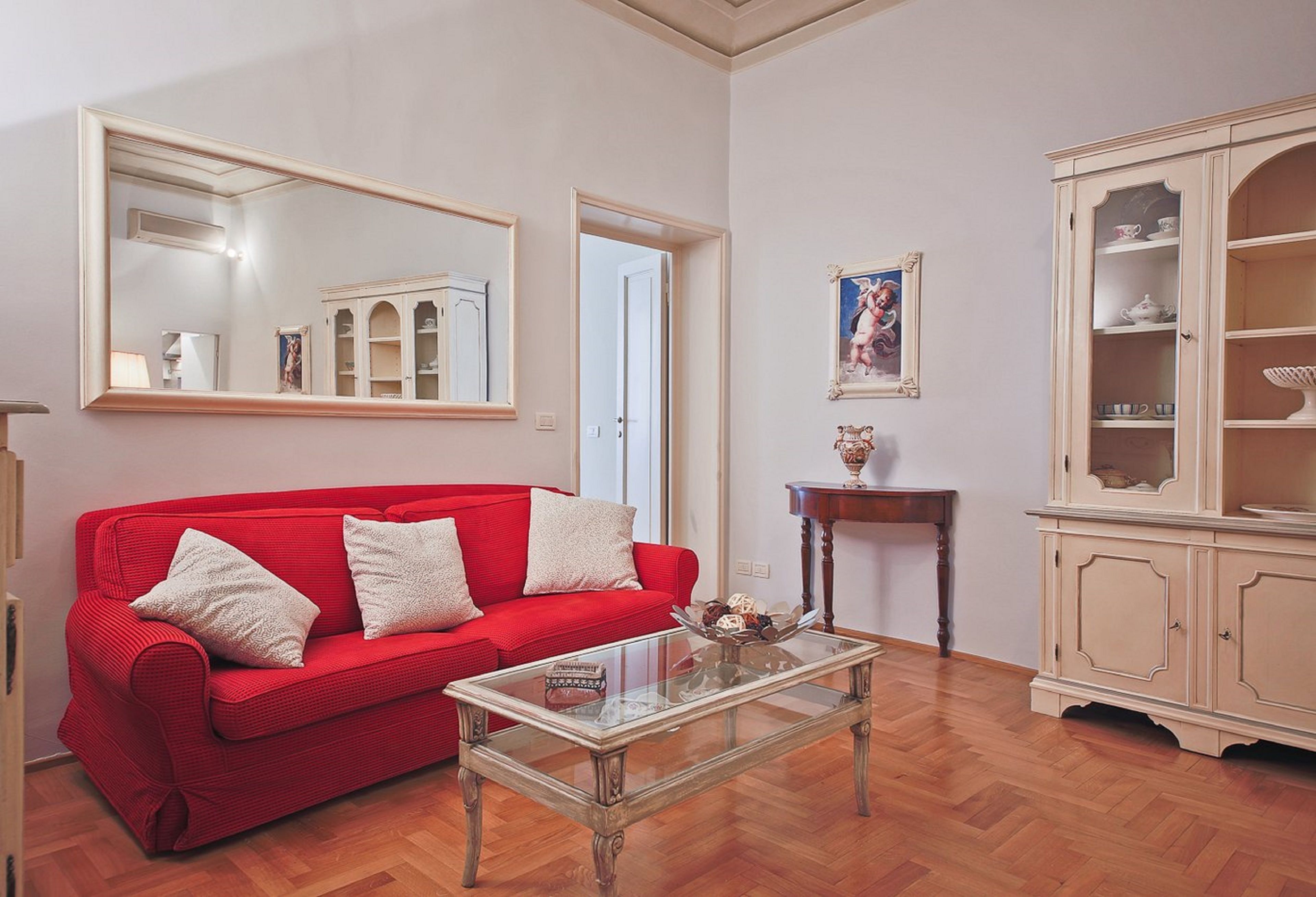 Ein Wohnzimmer mit einem roten Sofa, einem Glastisch, einem Holzschrank und einem großen Spiegel.