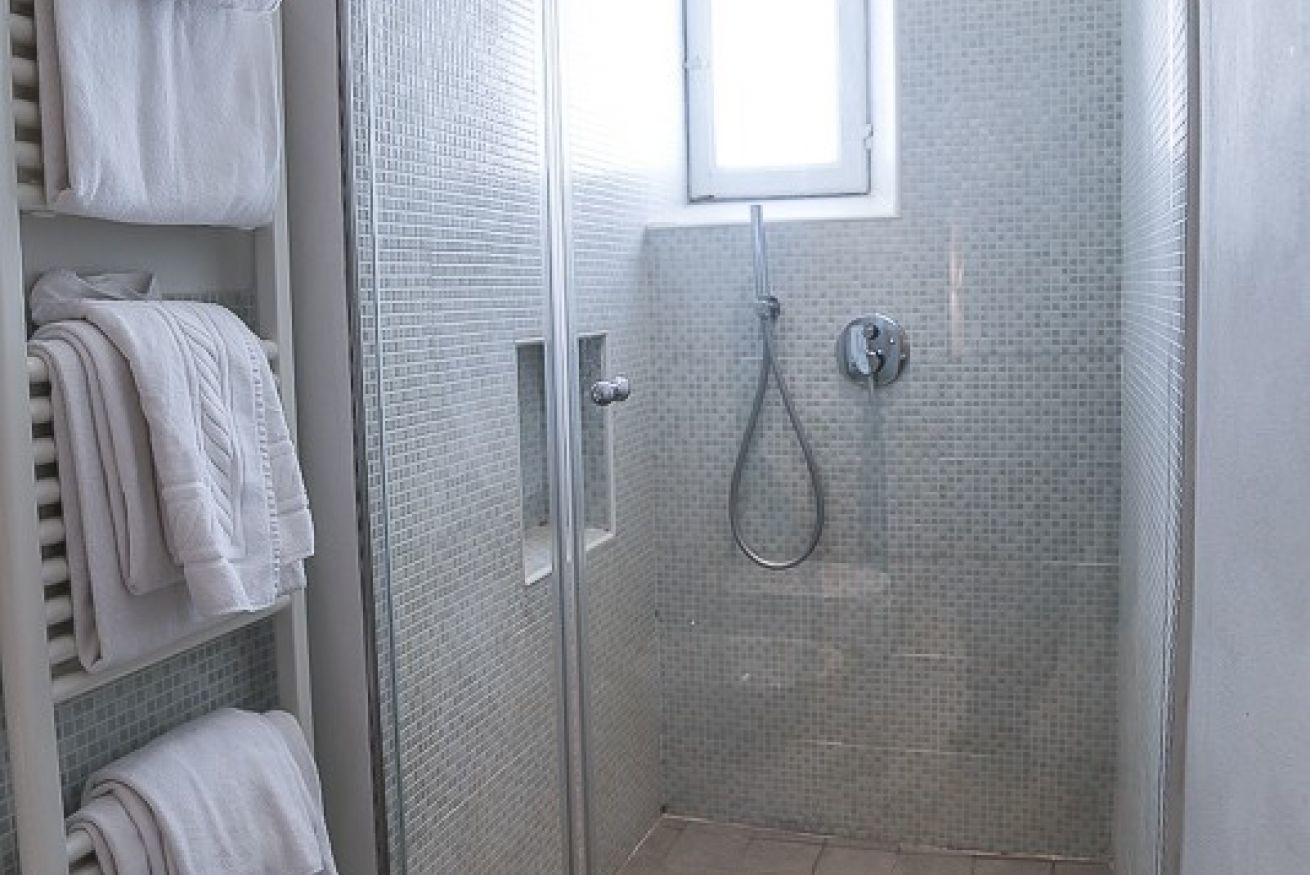 Una doccia a pavimento con porta in vetro, pareti piastrellate e una finestra sopra.