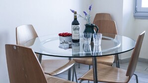 A round glass table with four wooden chairs, a bottle of wine, a pitcher with flowers, and a small vase with red flowers. - Ghibellina Loft (Florence)