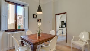 A dining area with a wooden table, white chairs, a hanging light fixture, and a view of the kitchen through an open door. - Ghibellina Michelangelo (Florence)