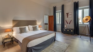 A spacious bedroom with a large bed, a wooden headboard, a nightstand with a lamp, and a dresser with a mirror. - Ghibellina Michelangelo (Florence)