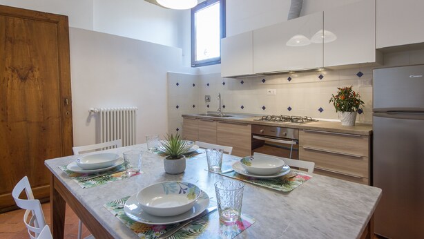 A modern kitchen with white cabinets, a stainless steel refrigerator, and a dining area with a table set for two. - House in Florence Blue (Florence)