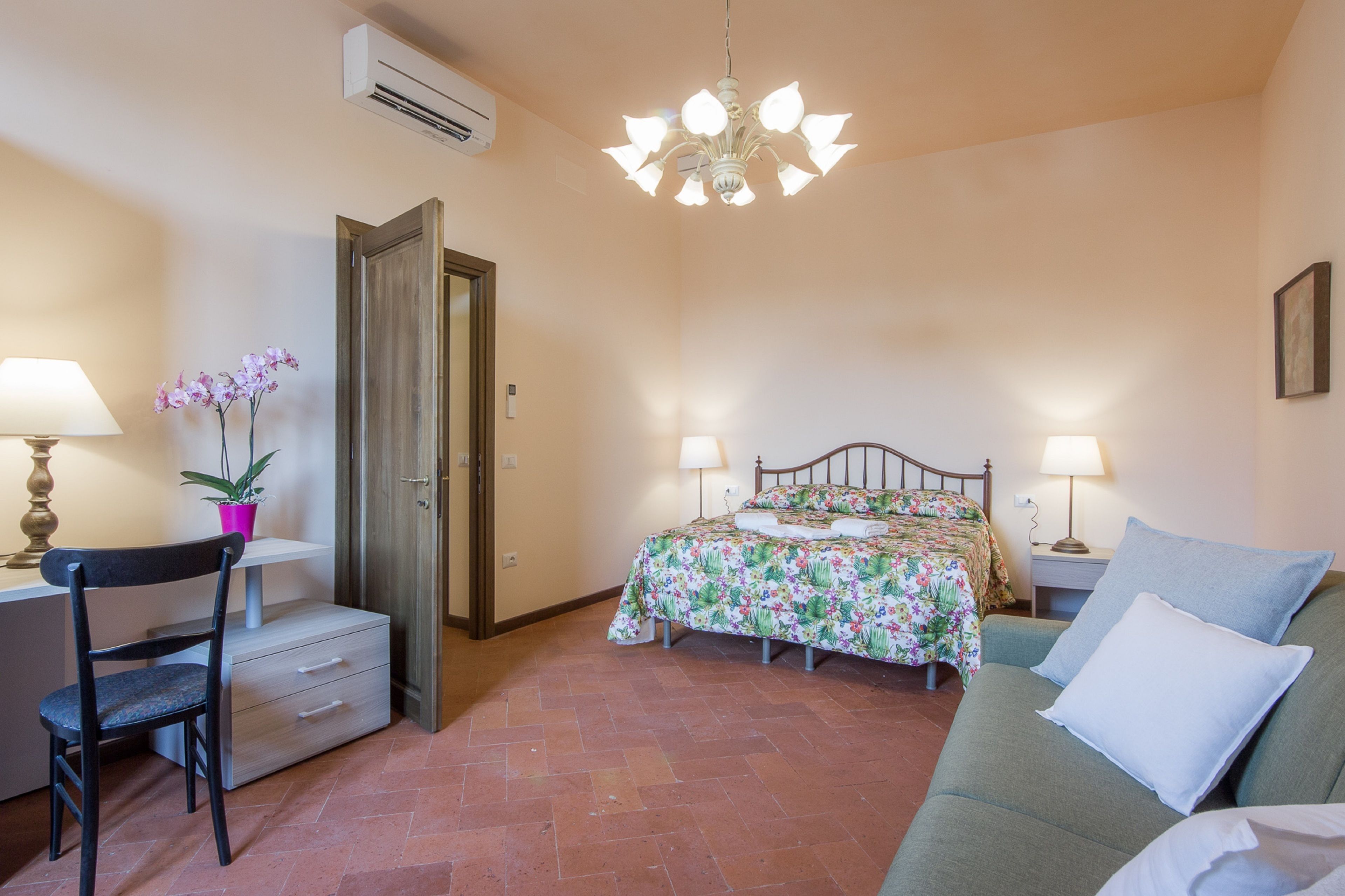A bedroom with a bed, two bedside lamps, a chair, a desk, and a small table with a plant.