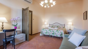 Ein Schlafzimmer mit einem Bett, zwei Nachttischlampen, einem Sessel, einem Schreibtisch und einem kleinen Tisch mit einer Pflanze.