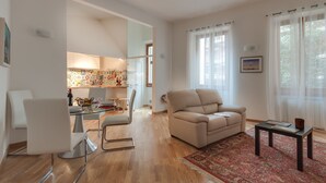 A modern living room with a beige sofa, a dining area with a glass table, and a kitchen visible through an open doorway. - Liberta Loft (Florence)