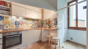 A kitchen with a gas stove, oven, and tiled backsplash. There are two stools and a window with a view. - Liberta Loft (Florence)