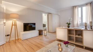 A modern living room with a flat-screen TV, wooden flooring, a lamp, a small table with candles, and a potted plant.