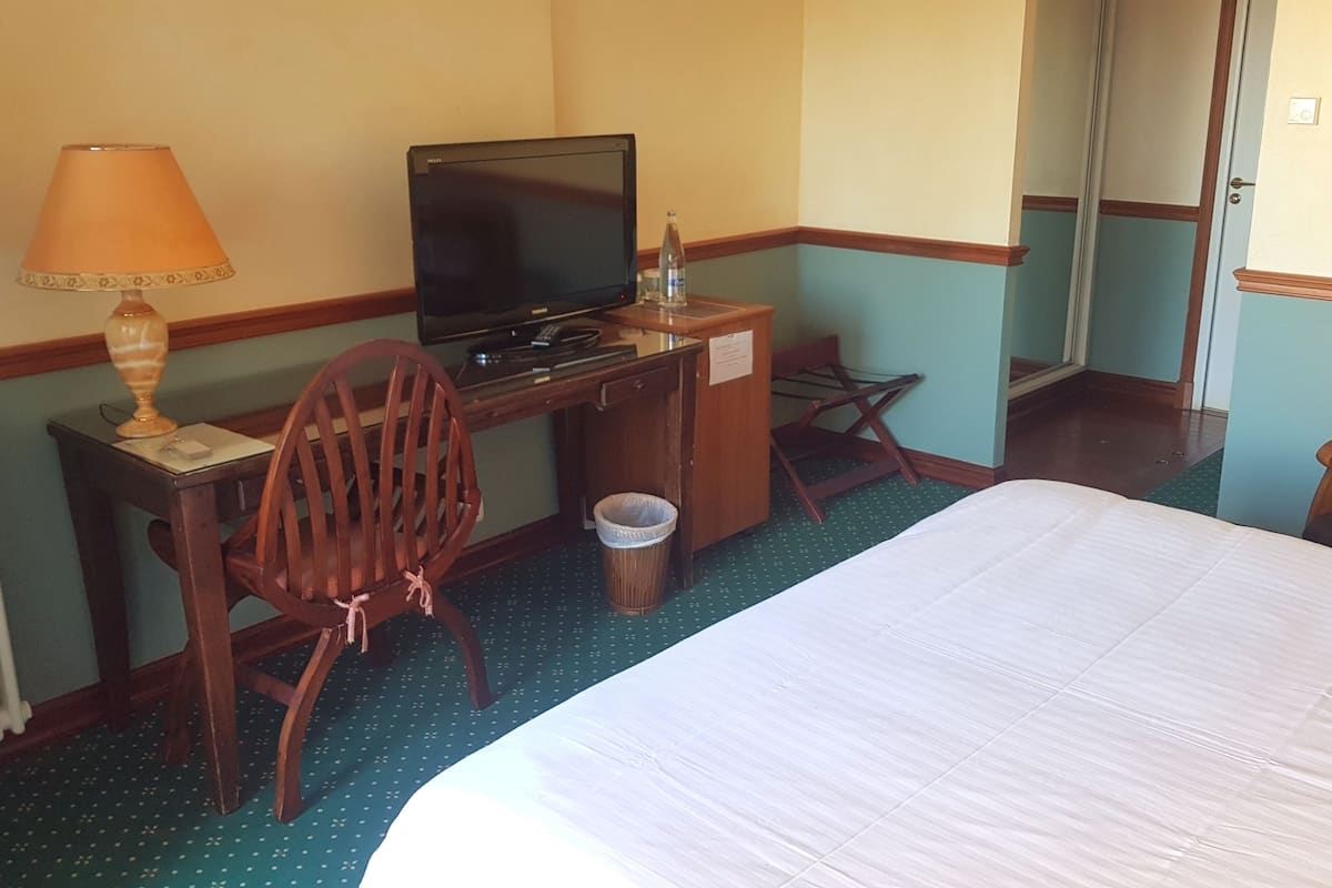 Una habitación de hotel con una cama, un escritorio con televisor, una silla, un cesto de basura y una lámpara.