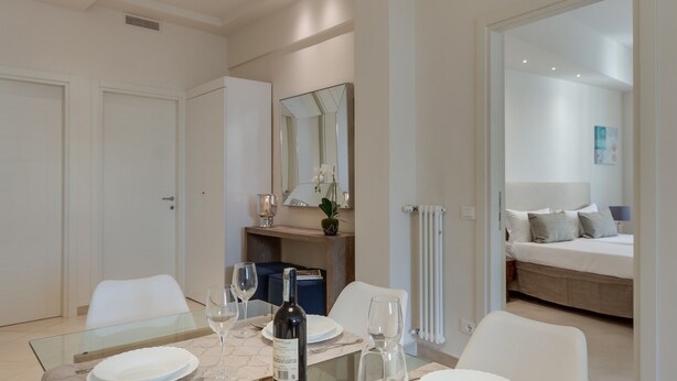 Ein modernes Hotelzimmer mit Essbereich, einem großen Bett und einem durchgegangenen Tür erkennbaren Badezimmer.