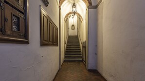 Un couloir étroit doté d’un plancher en bois, d’un escalier et d’un luminaire fixé au mur.