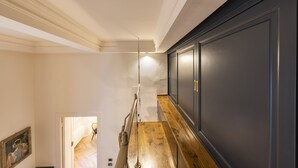 Un escalier en bois mène à une porte sombre, un luminaire est fixé au-dessus, et un tableau encadré orne le mur.