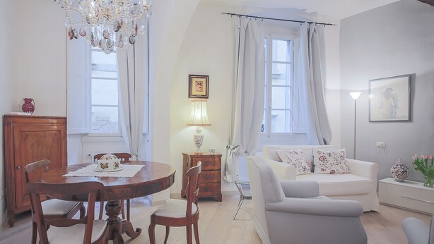A dining area with a wooden table and chairs, a chandelier, and a window with curtains. - Parione (Florence)