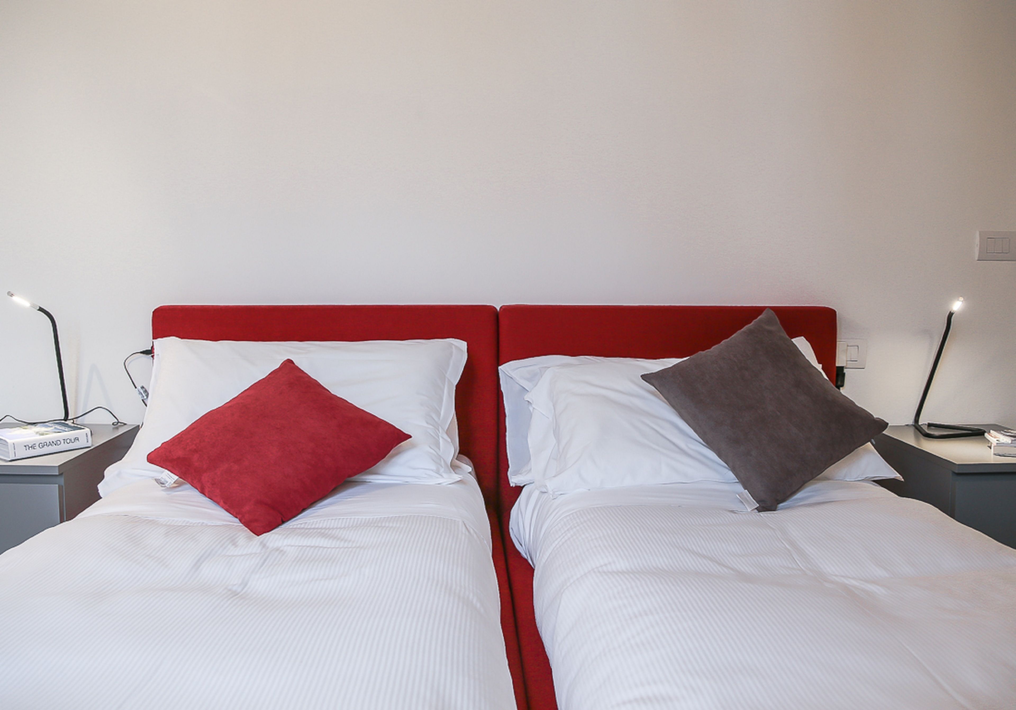 En dobbeltseng med rødt sengegærde og to puder, en rød og en grå, i et hotelværelse.