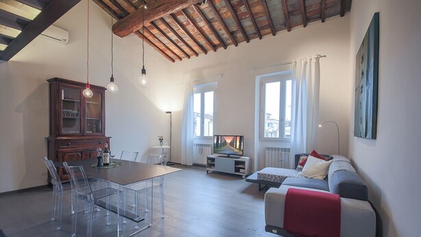 A spacious living area with a wooden ceiling, a dining table with chairs, a sofa, and a television. - Pepi Loft (Florence)