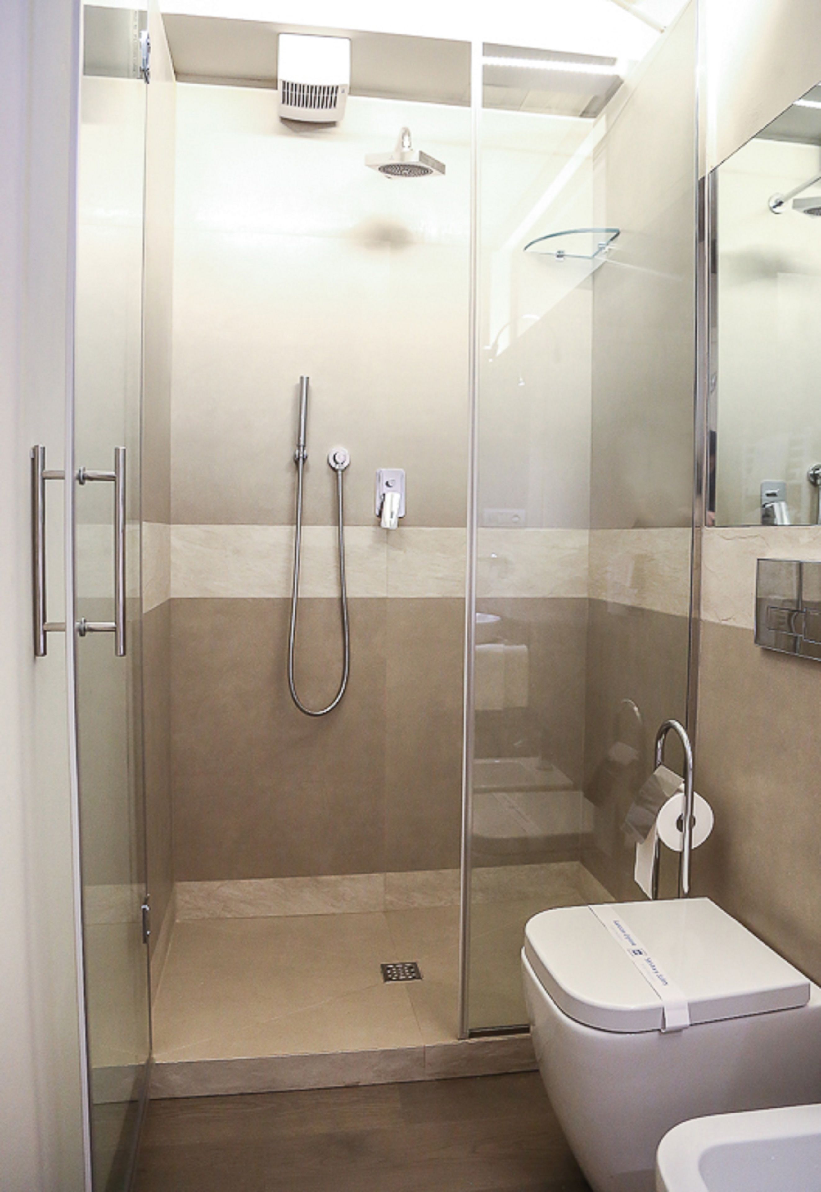 A glass-enclosed shower stall with a handheld showerhead and a wall-mounted faucet.