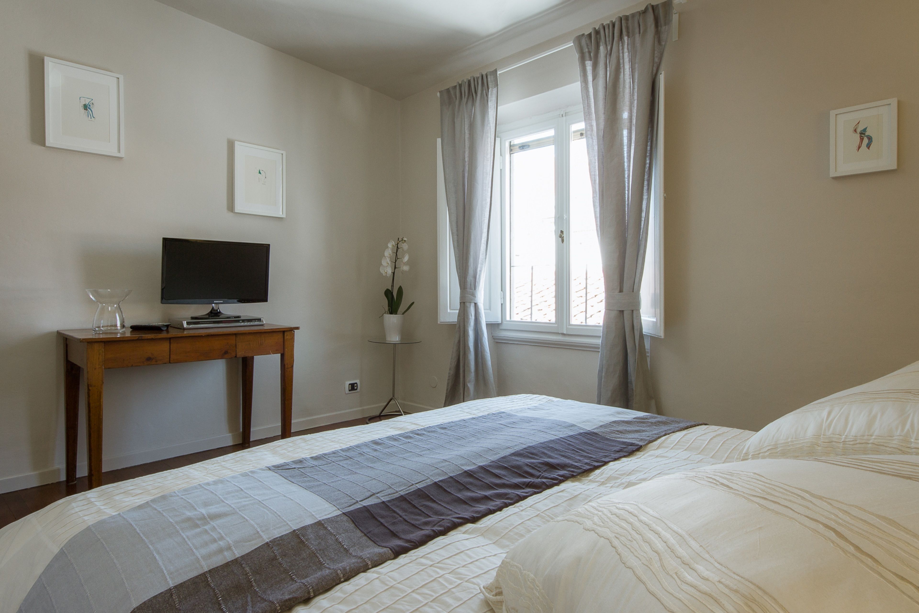 A bedroom with a bed, a TV on a wooden table, and a window with curtains.