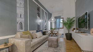 Een moderne woonkamer met een grijze bank, een bijzettafeltje en een grote potplant.