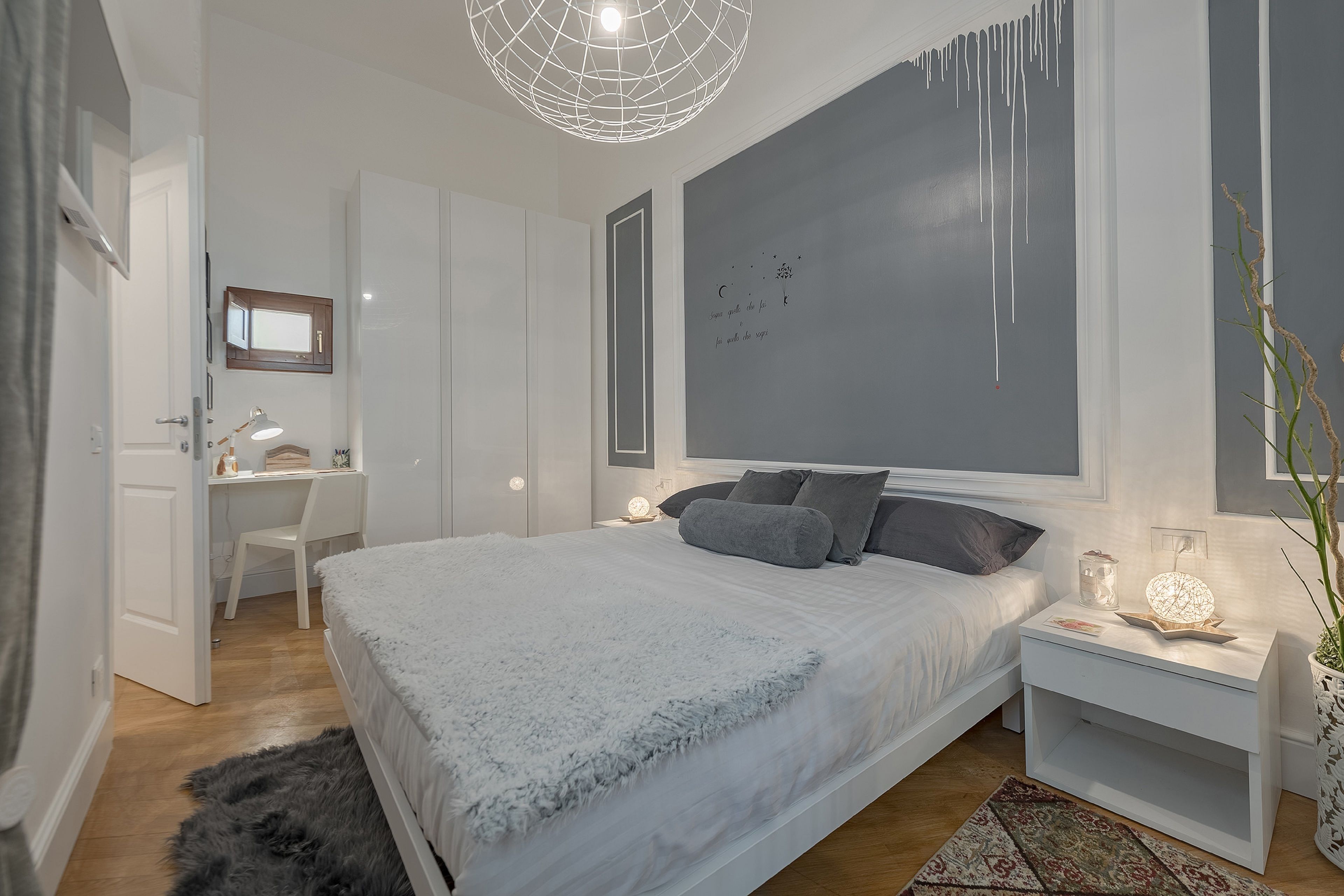 Ett modernt sovrum med en stor säng, sängbord, ett skrivbord och en vägg med en dekorativ lampa.