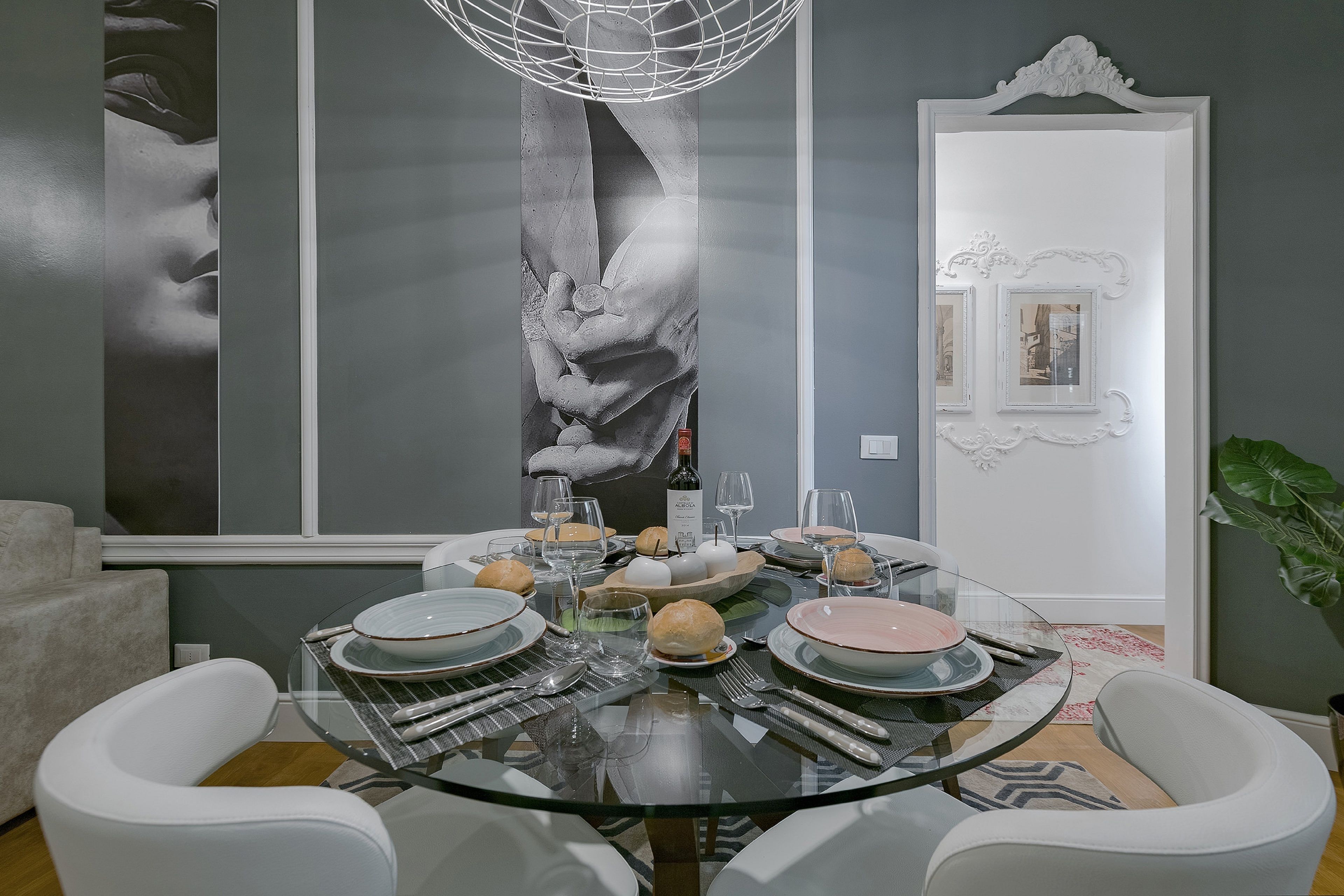 A dining area with a glass table, white chairs, and a large abstract painting on the wall.