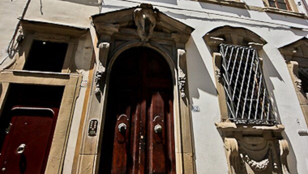 A multi-story building with a central entrance featuring a wooden door and an ornate stone archway. - Pergola in Palazzo Leopardi (Florence)