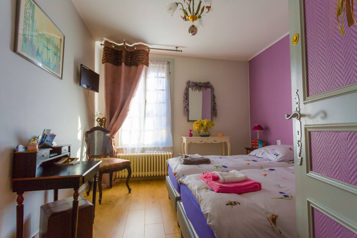 Une chambre à coucher comprenant un lit, un bureau, une chaise, un radiateur, un téléviseur et une porte.