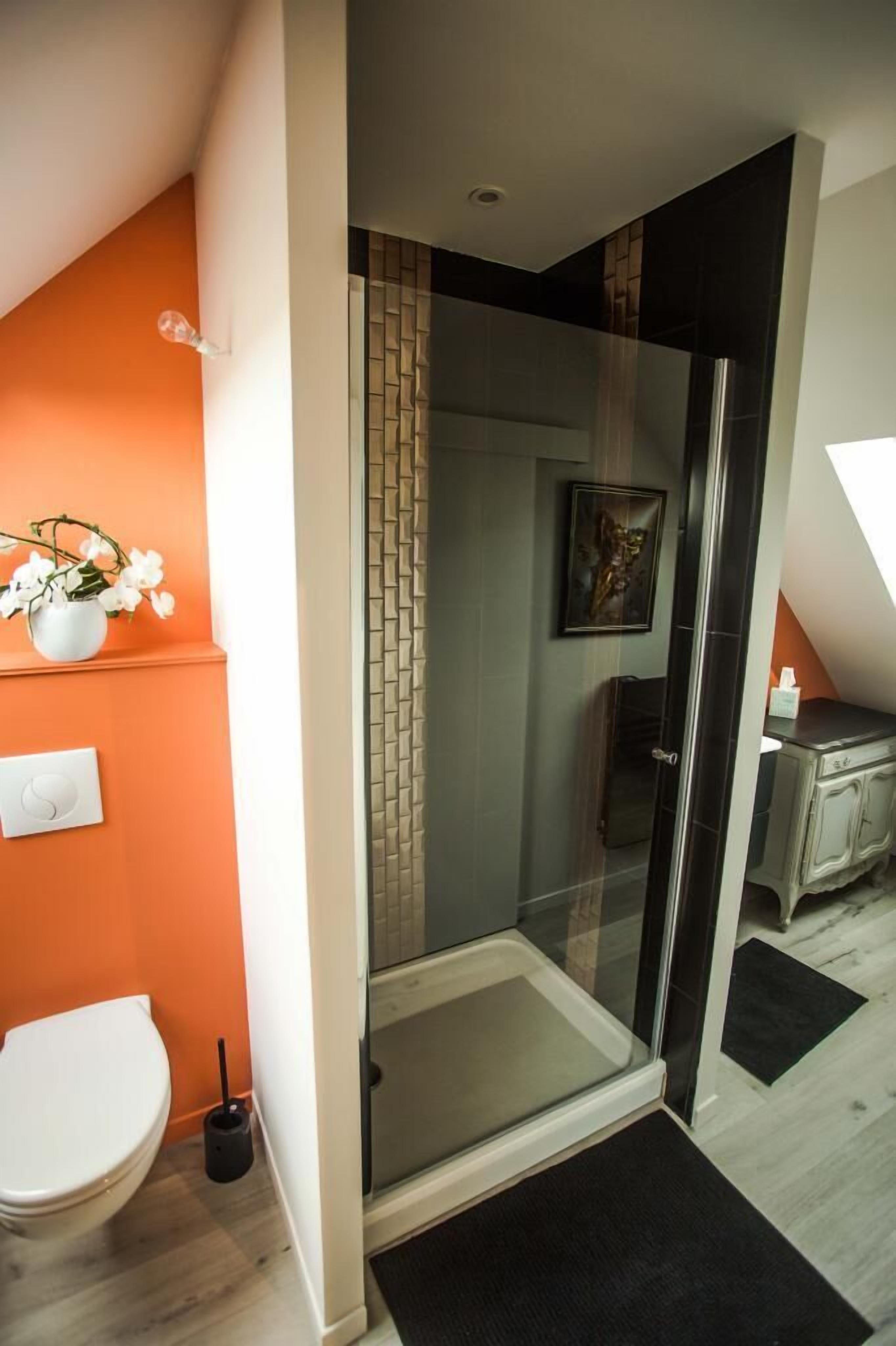 A modern bathroom with a glass shower enclosure, a white toilet, and a small sink area.